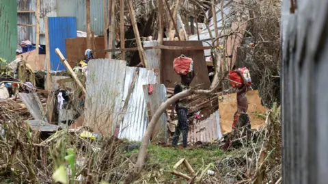 Reuters Two people are seen carrying bags on their heads amid strewn tin panels and timber from destroyed shacks