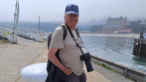 Fred Tiles A man in a blue cap and brown t-shirt standing by the pier at Scarborough.