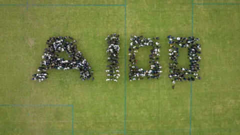 Greybox Geospatial Ltd An aerial shot of students standing on a school sports field spelling out the figures 'A100' 