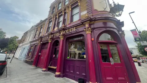 Exterior shows purple Queen of the South pub with double doors and glass windows