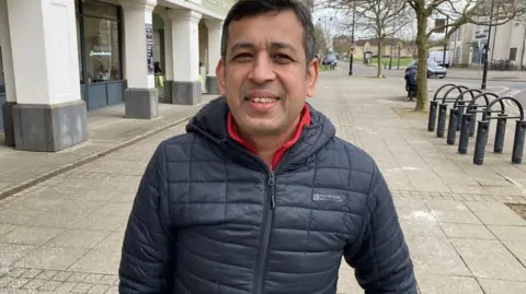 Jozef Hall/BBC Hasan Mustafa in a puffer jacket, standing in Cambourne