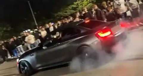 SNAP Footage from the car meet of a black car skidding its tyres in front of a large crowd.