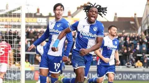 Bristol Rovers FC Three Bristol Rovers players celebrate after scoring a late equaliser against Wrexham at the Memorial Stadium. Goalscorer Promise Omochere is leading the celebrations