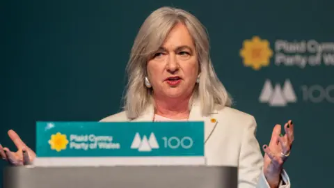 Plaid Cymru Liz Saville Roberts stood giving a speech at Plaid Cymru conference, in front of the party's logo