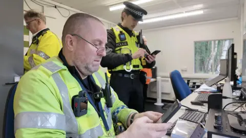 Two police officers on devices checking the legal status of vehicles.