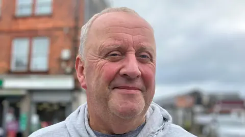 Man in grey hoodie in front of buildings in Callington 