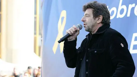 French singer and actor Patrick Bruel speaks through a microphone during a rally in 2025