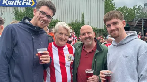 supplied A family of four pose together holding pints. Mum and Dad are in the middle with two large sons flanking them on each side