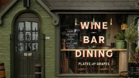 Harry Parkinson A brick building that has been painted green with a dark green door and a large window. The window has the words "wine bar dining" and "Plates and Grapes" painted onto it.