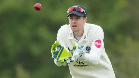 Robbie White catches the ball with his gloves, playing at wicketkeeper