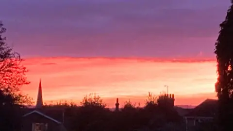 ELIE/WEATHERWATCHERS A grainy image of the tips of homes in Linslade, Bedfordshire, underneath a sky which is one half pink and one half piurple