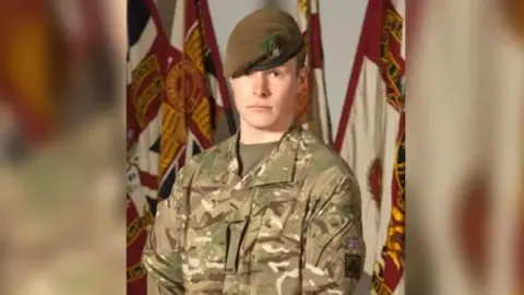 MOD A young soldier wearing camouflaged fatigues. He is wearing a dark green beret and cap badge of The Yorkshire Regiment. 