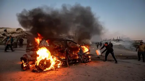 A Palestinian man attempts to put out the fire that engulfed a car after an Israeli drone strike the killed Mohammed Wishah, a correspondent for Al Jazeera Mubasher, and one other person, in Gaza City, northern Gaza (8 April 2026)