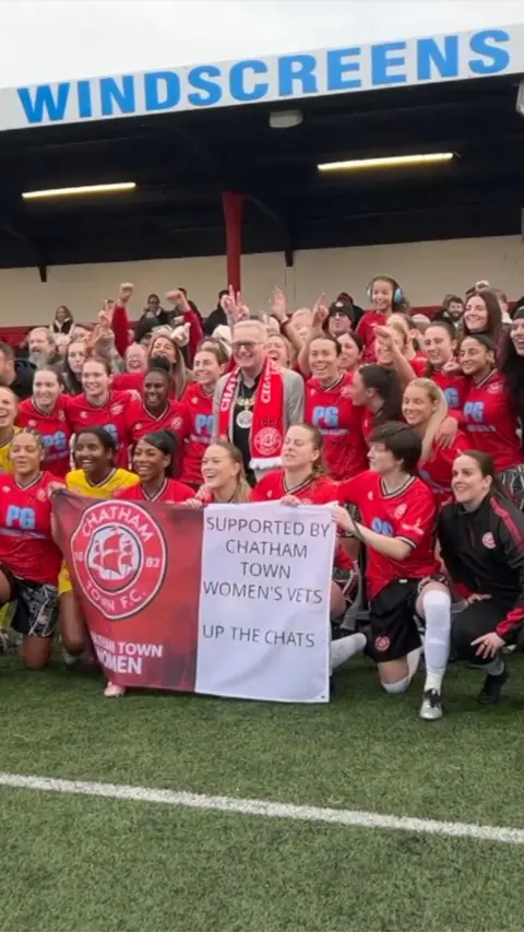 Women in red kit celebrate and pose in a football stadium 