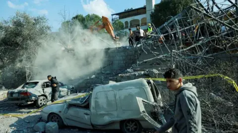 Reuters men are seen next to damaged vehicles at the site of an Israeli air strike near Byblos