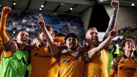 Mohamed Belloumi and Oliver McBurnie of Hull City celebrate at full time following the team's victory in the Championship play off semi-final second leg match against Millwall. They are joined by other players and all are wearing orange football shirts.