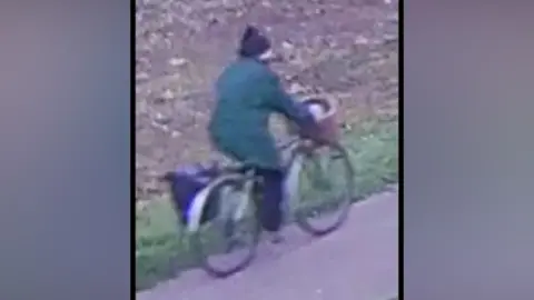 Eastern Region Special Operations Unit A person wearing a green coat and black woolly hat rides a bike in grainy CCTV footage. 