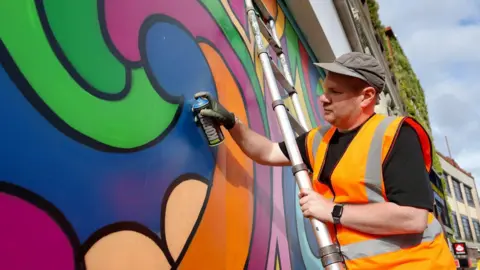 Bournemouth Arts by the Sea Festival A man with a spray can in a high vis jacket spraying paint on a wall.