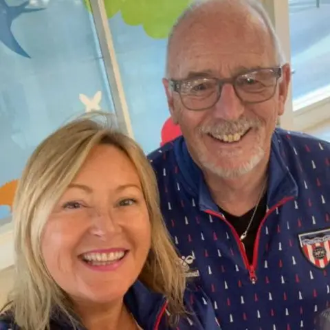 Sunderland AFC's Heaven Supporters Branch Joanne Youngson smiling with shoulder length blonde hair and blue football top. Billy Wright with some white hair at the sides and a short white beard. He is wearing glasses and smiling. He is also wearing a blue football top.