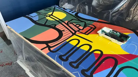 LDRS Multicolour mural with black lines depicting abstract monuments laid on a table