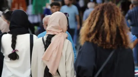 EPA-EFE/REX/Shutterstock Three Iranian women, one wearing a black head covering, another with a pink hijab and  a fourth one without a head covering with thick curly brown hair, walking. 