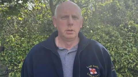 Joe Joyce, he has white hair and wearing a navy jacket that says Lough Swilly Lifeboat crew. He is wearing a grey polo shirt.
