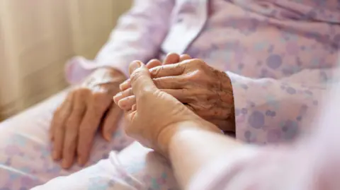 A close-up of an elderly woman holding hands with a visitor