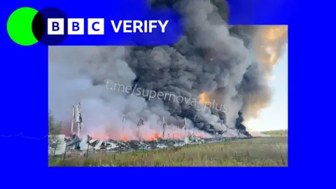 A BBC Verify graphic next to an image of a huge plume of smoke rising from the remains of a building.