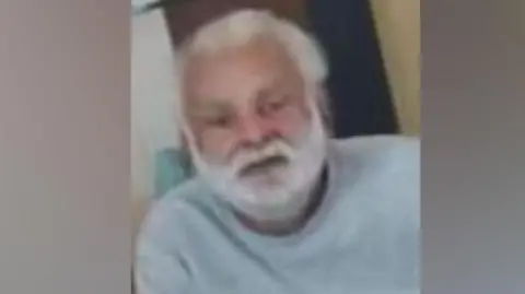 Sukhjinder Singh-Gill: A man with white hair and and white beard wearing a pale grey, round-necked. long-sleeved, top.