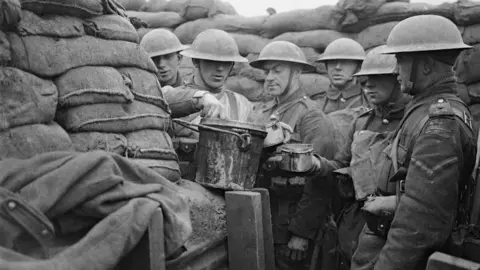Imperial War Museum A black and white picture of soliders in trenches surrounding a pot.