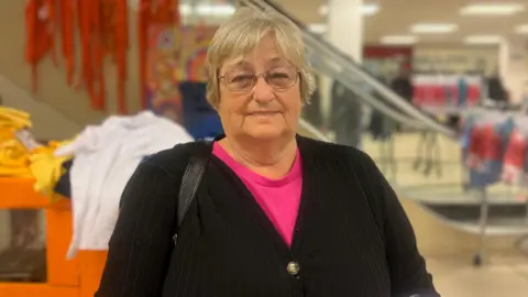 Jasmine DuFraisse/BBC Sandra Turton is wearing glasses, has short grey hair and is wearing a pink top with a black cardigan.