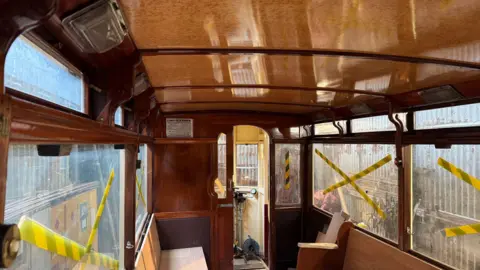 The inside lower deck of a restored tram carriage with dark wood panels and window frames and a light vinyl roof