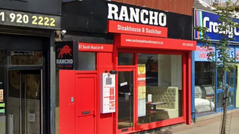 The outside of a restaurant with its fascia and shop front painted in a black and red theme. A sign has a logo of a bull about to charge. 