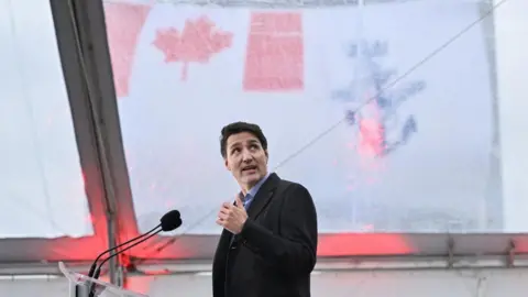 Justin Trudeau looks up as he stands before a microphone wearing a dark coat