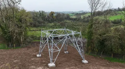 Four base legs of an metal electrical pylon built in a mud field.