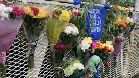 Phil Bodmer/BBC Flowers attached to the side of a bridge. A blue school jumper is in the middle.