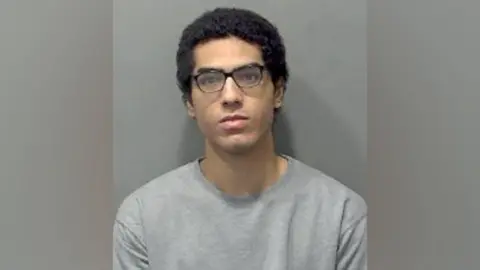 Bedfordshire Police Nicholas Prosper, who has acheronian  hairsbreadth  and acheronian  glasses, staring into the camera for a constabulary  custody image