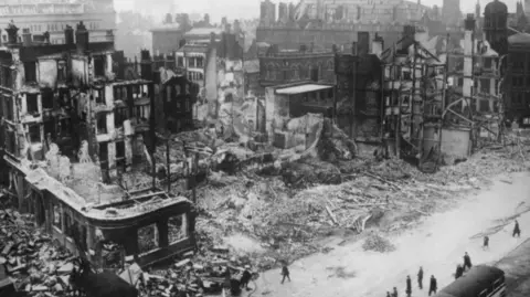 A black and white photo showing extensive damage to a building which has partially collapsed into rubble after being struck in the bombing raid 