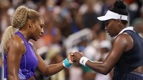 Serena Williams bumps fists with Venus Williams during their first round match at the Cincinnati Open