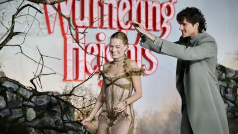 WireImage/GettyImages Jacob Elordi puts his hands above Margot Robbie's head in an attempt to shield her from the rain as they both smile.