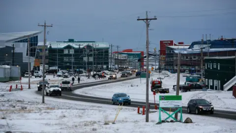 Getty Images A road in Iqaluit that shows several buildings, various cars on the road, lots of power poles and somewhat light snow on the ground.