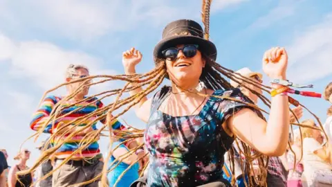 Wychwood Festival A woman with dreadlocks wearing a starry dress and sunglasses is dancing.