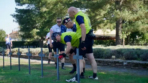 Three men looking at a metal cross in a cemetery