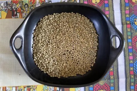 A black pan filled with pale green coffee bean sitting on top of a colourful table cloth. 