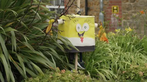 A scarecrow of Spongebob Squarepants sticking out of a bush