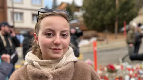 Blonde-haired Lea Zehnder looks into the camera wearing a woolen hood and a fur-look coat