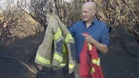 BBC South environment correspondant in the New Forest holding two different firefighter jackets.