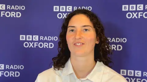 Miriam Pritchard smiling for a picture against a purple BBC-branded wall.