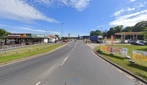 A road with a McDonald's to the left and a petrol station to the right. There is a lorry on the petrol forecourt and it is a clear, sunny day.
