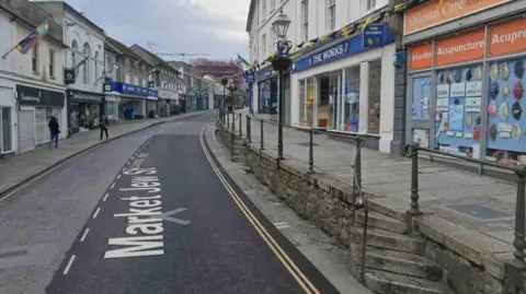 Google A street with shops and a pavement either side.